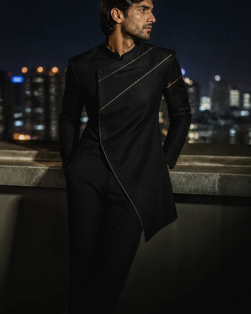 Man in a black asymmetric indo-western jacket against city lights